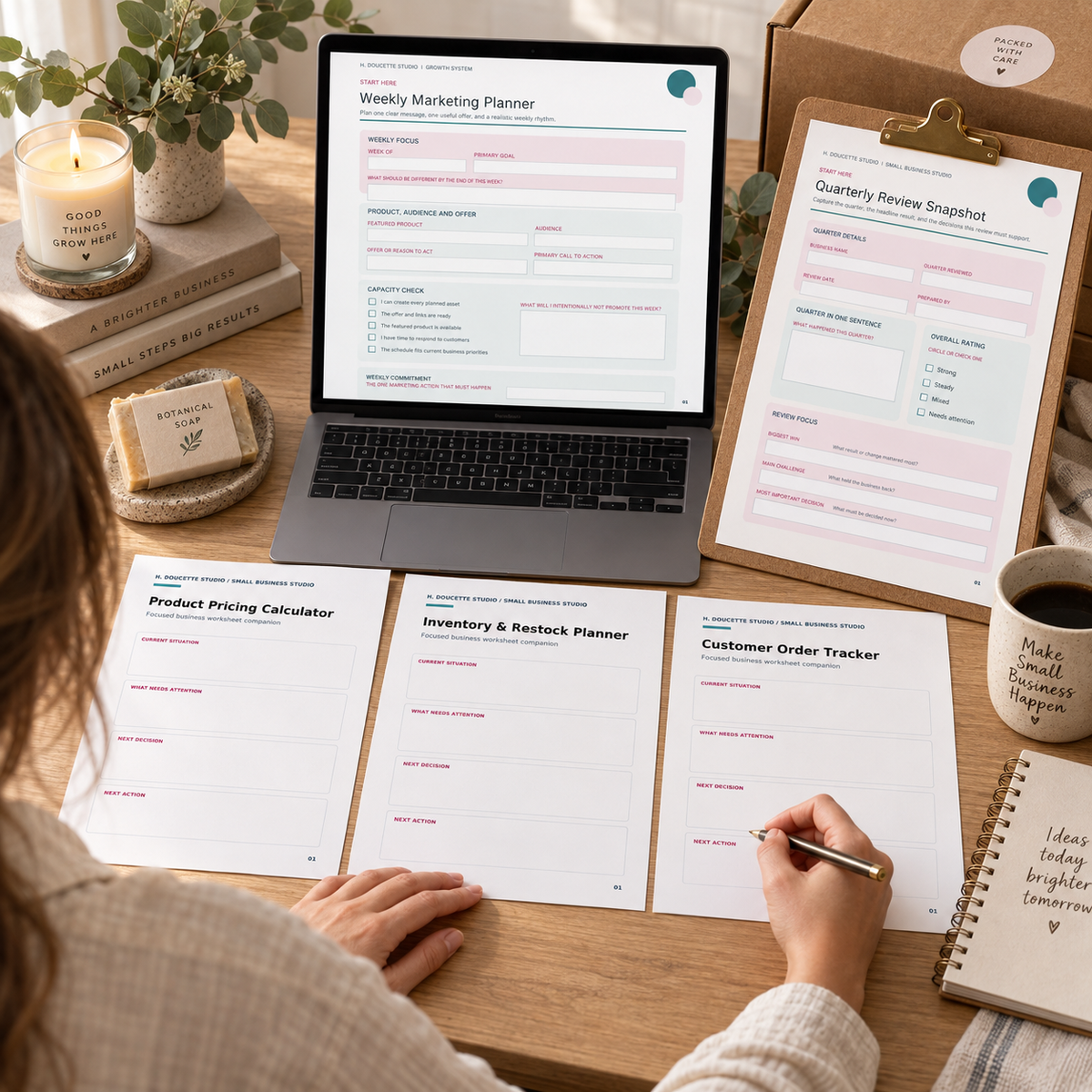 Small-business owner using all five Starter Bundle planners at a maker studio desk with exactly two matching sleeves and hands.